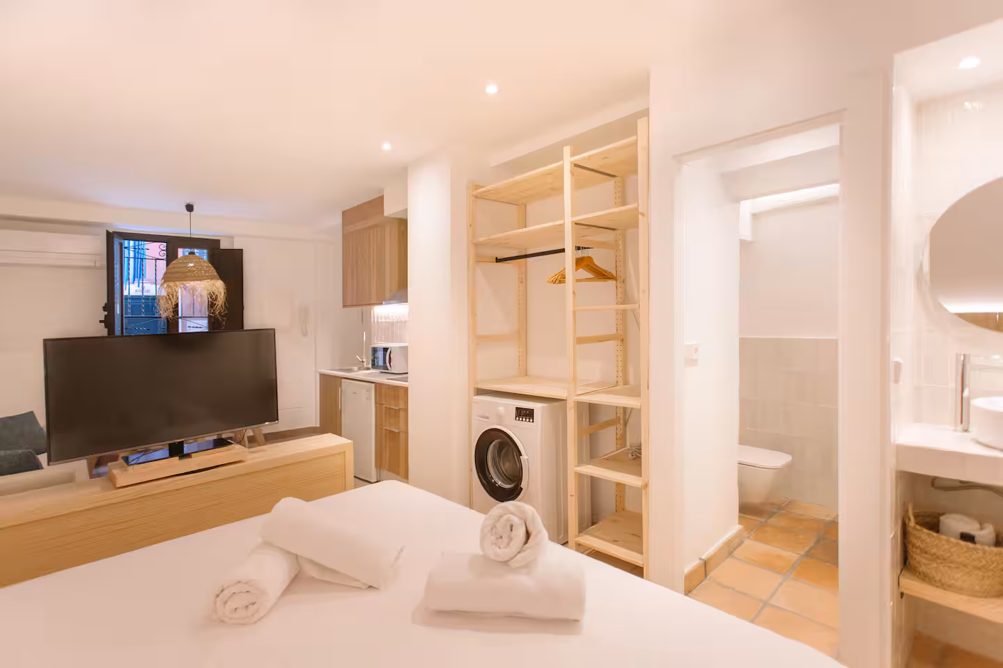 Vista general del apartamento con televisión, armario abierto y acceso al baño