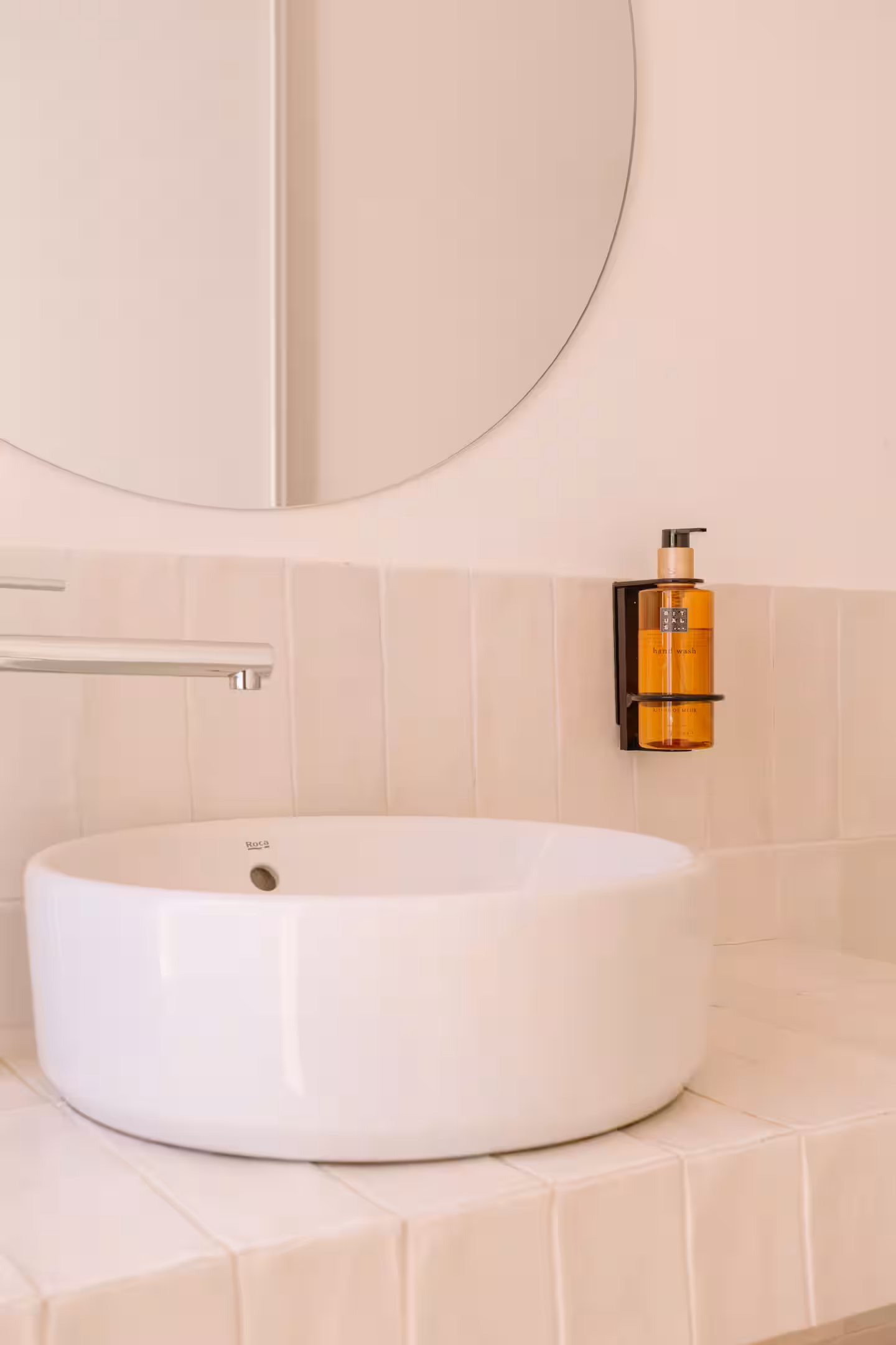 Lavabo circular de porcelana sobre encimera de obra con espejo redondo