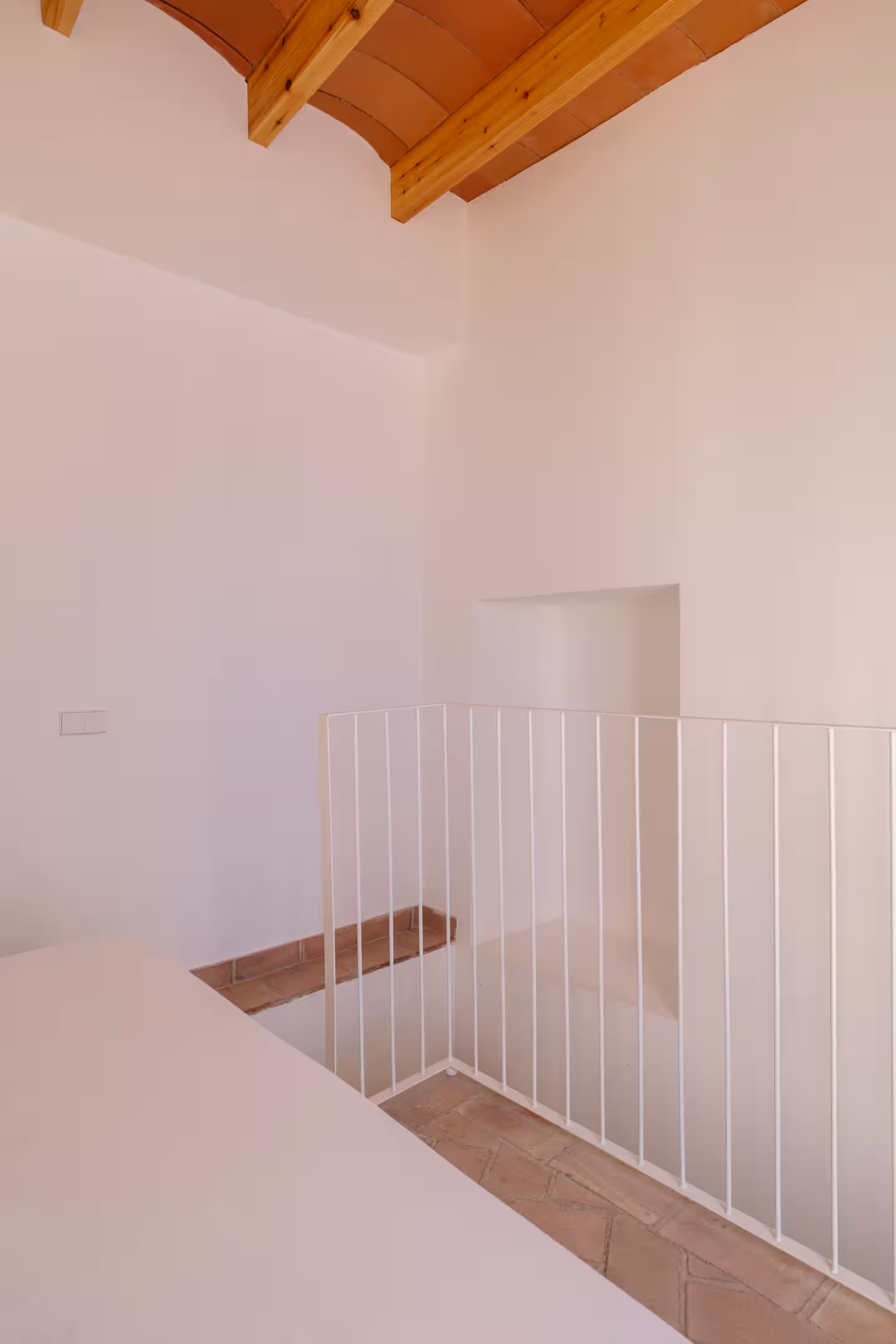 Escalera de obra con barandilla blanca hacia los dormitorios y techo de vigas de madera