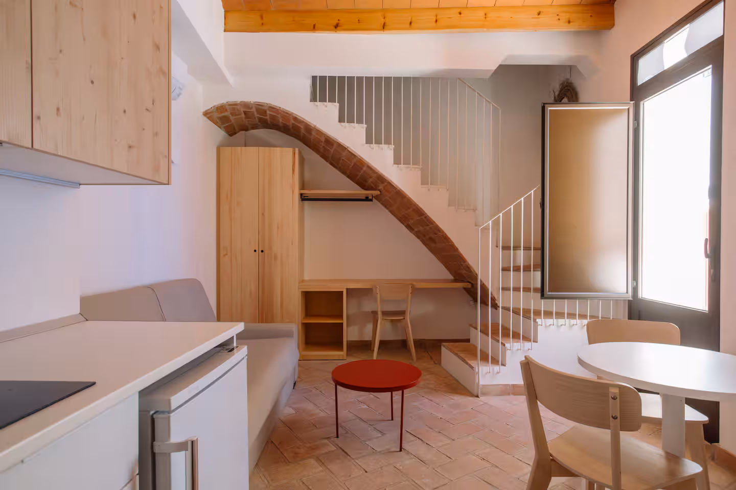 Salón de Mayor 36 con el arco de ladrillo original bajo la escalera, suelo de barro cocido y mesa auxiliar roja