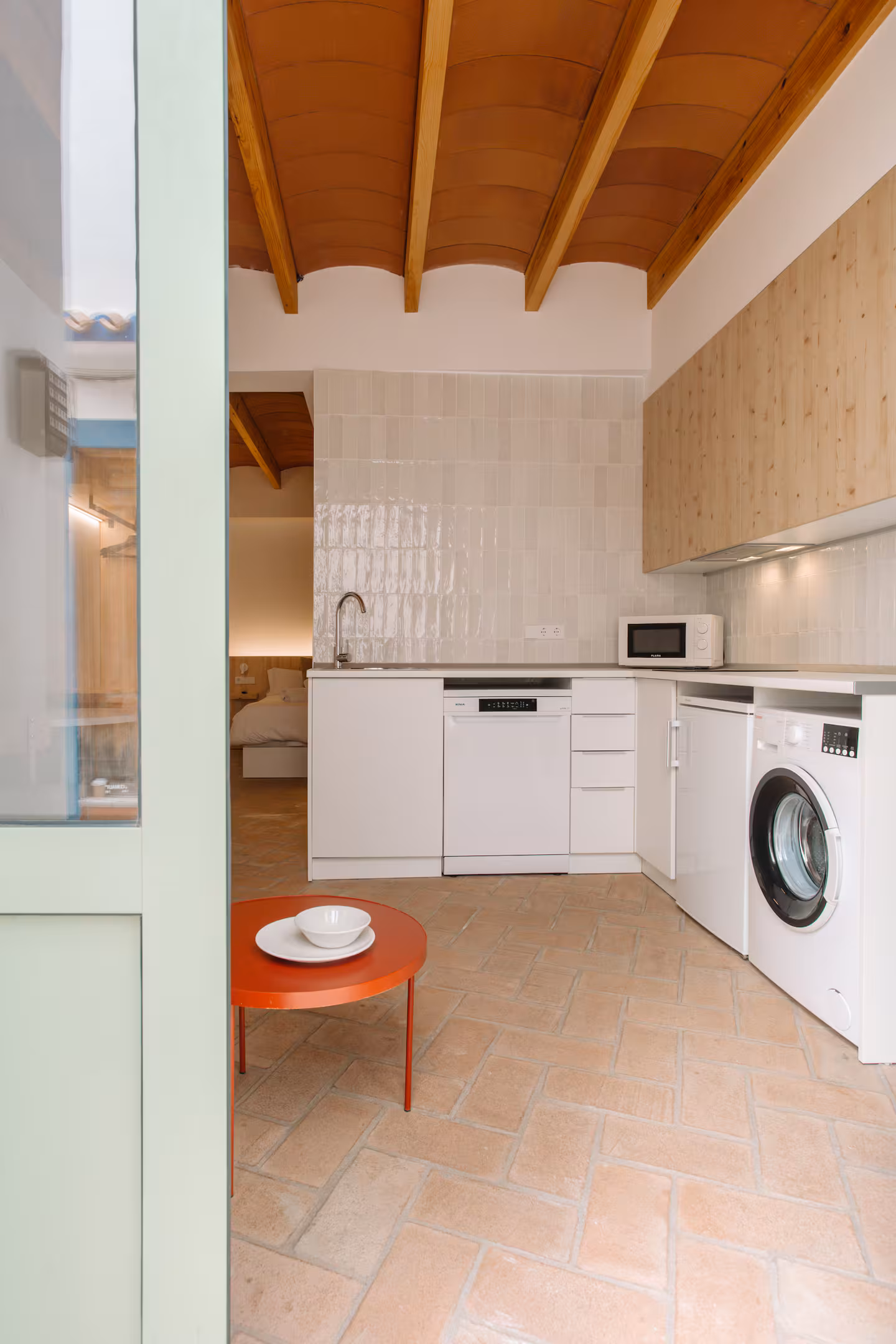 Cocina en enfilada vista desde el recibidor, con la puerta verde de entrada al fondo