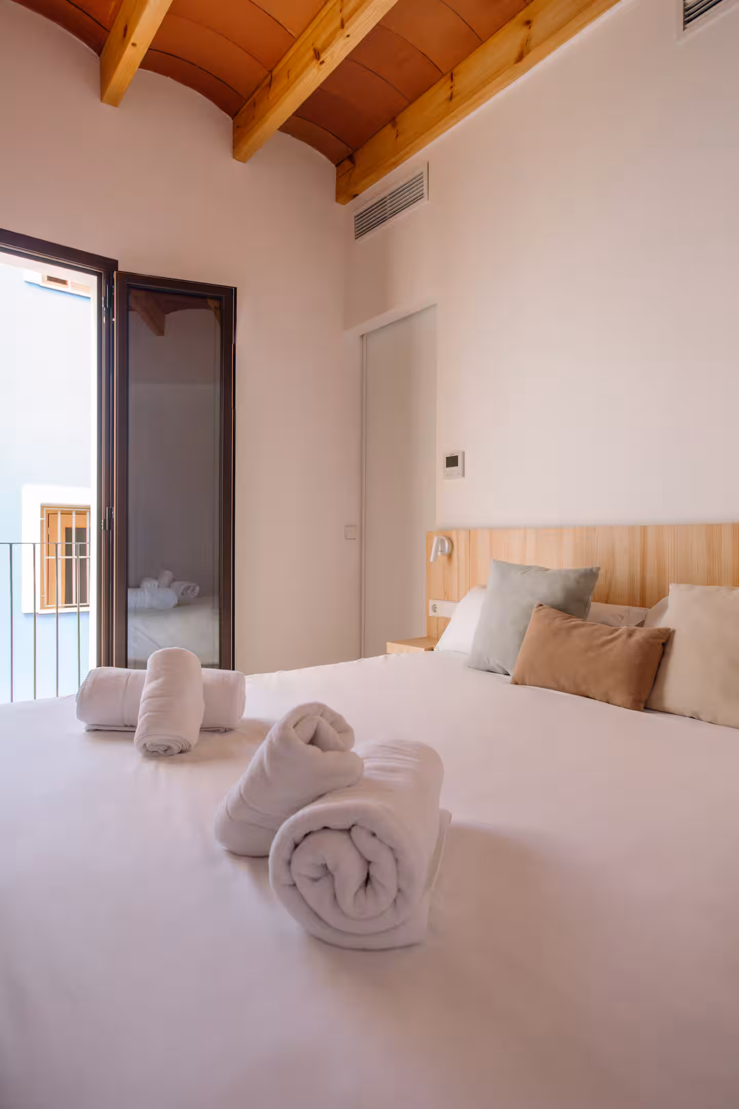 Cama con toallas enrolladas y salida al balcón del dormitorio