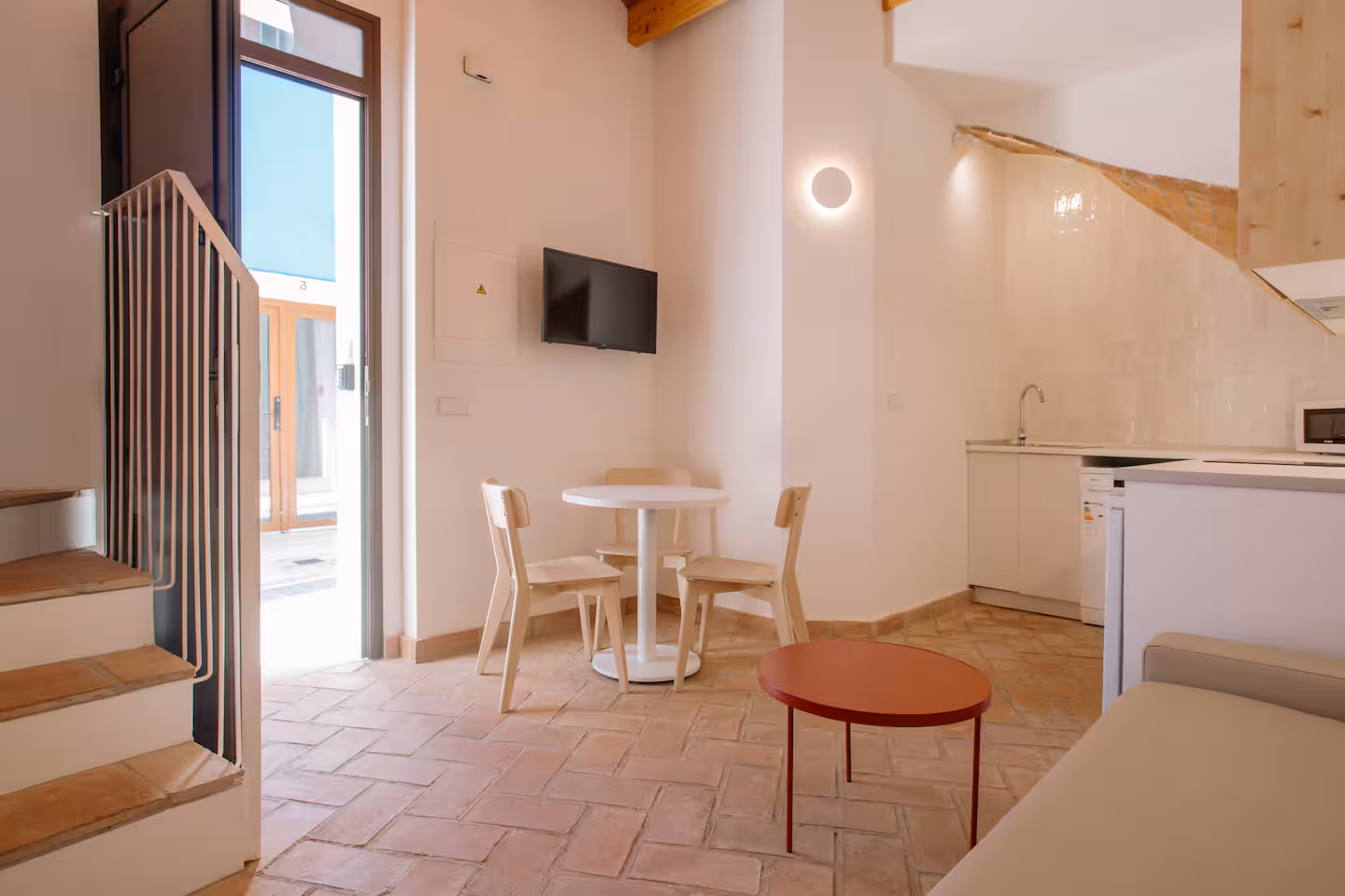 Comedor junto a la escalera con mesa, sillas de madera y televisión sobre la pared encalada