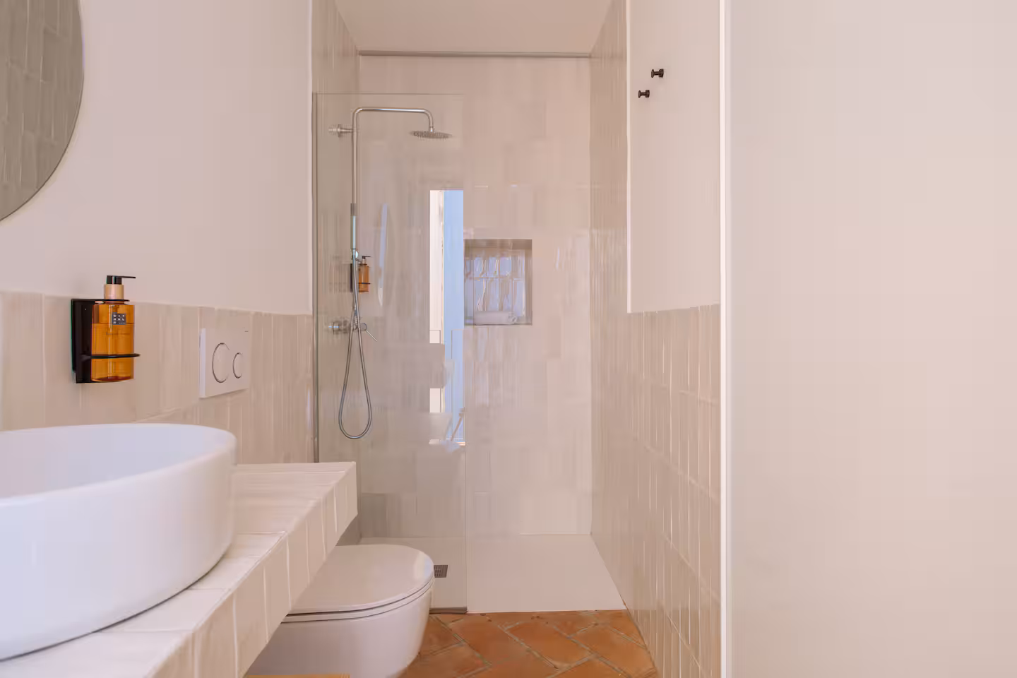 Baño completo con ducha a ras de suelo y lavabo circular junto a la ventana