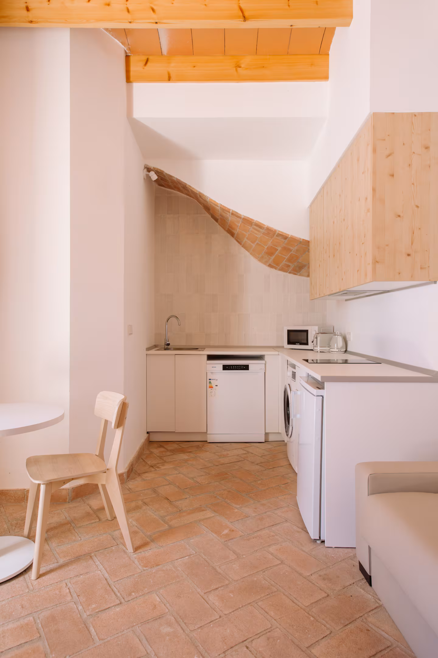 Cocina blanca bajo el arco de ladrillo con sofá claro en primer término