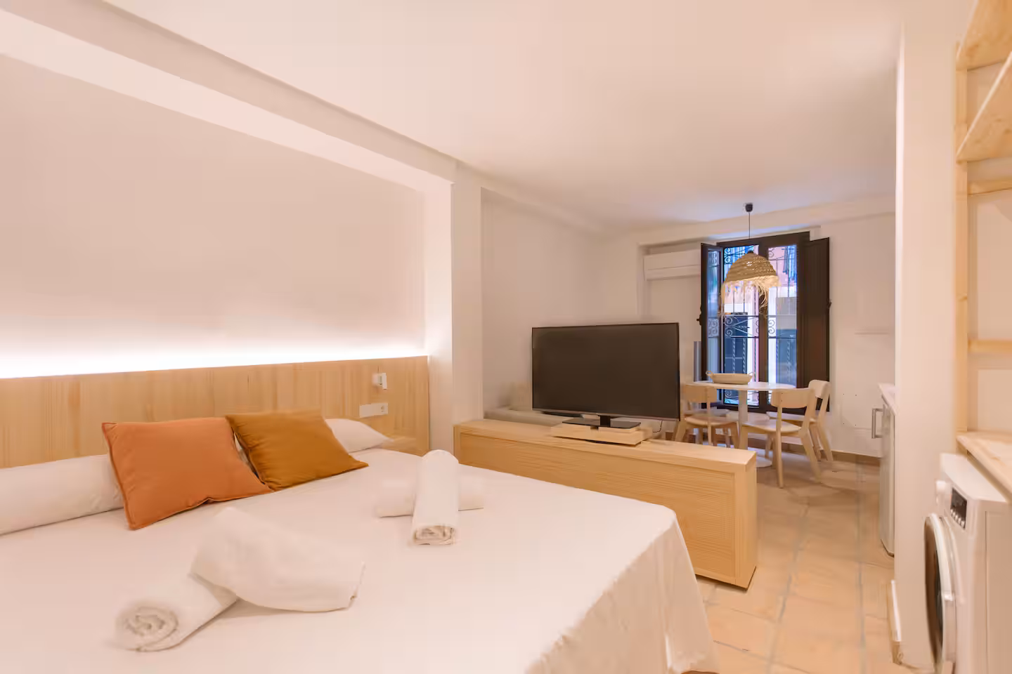 Zona de dormitorio con cojín naranja, televisión y ventana a la calle