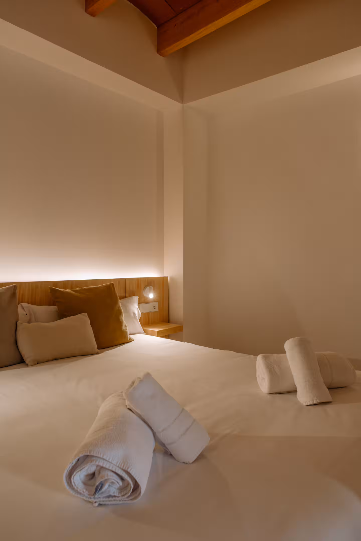Dormitorio bajo cubierta con toallas dobladas sobre la cama y luz cálida indirecta