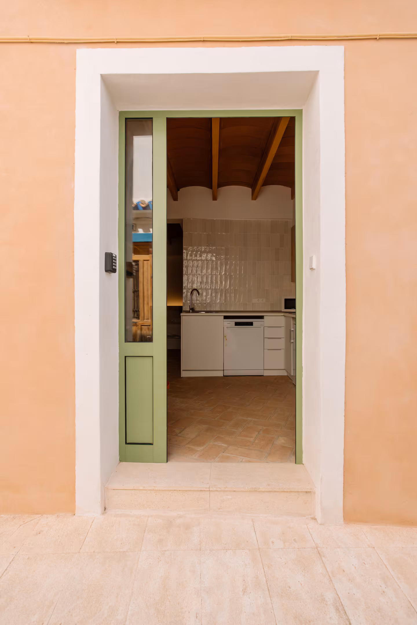 Puerta verde abierta desde la calle mostrando el interior encalado de la vivienda